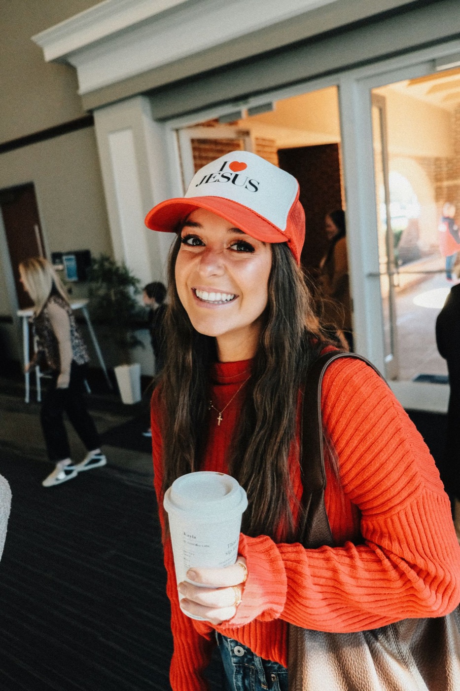 A smiling young woman in an I love Jesus cap holding a coffee
