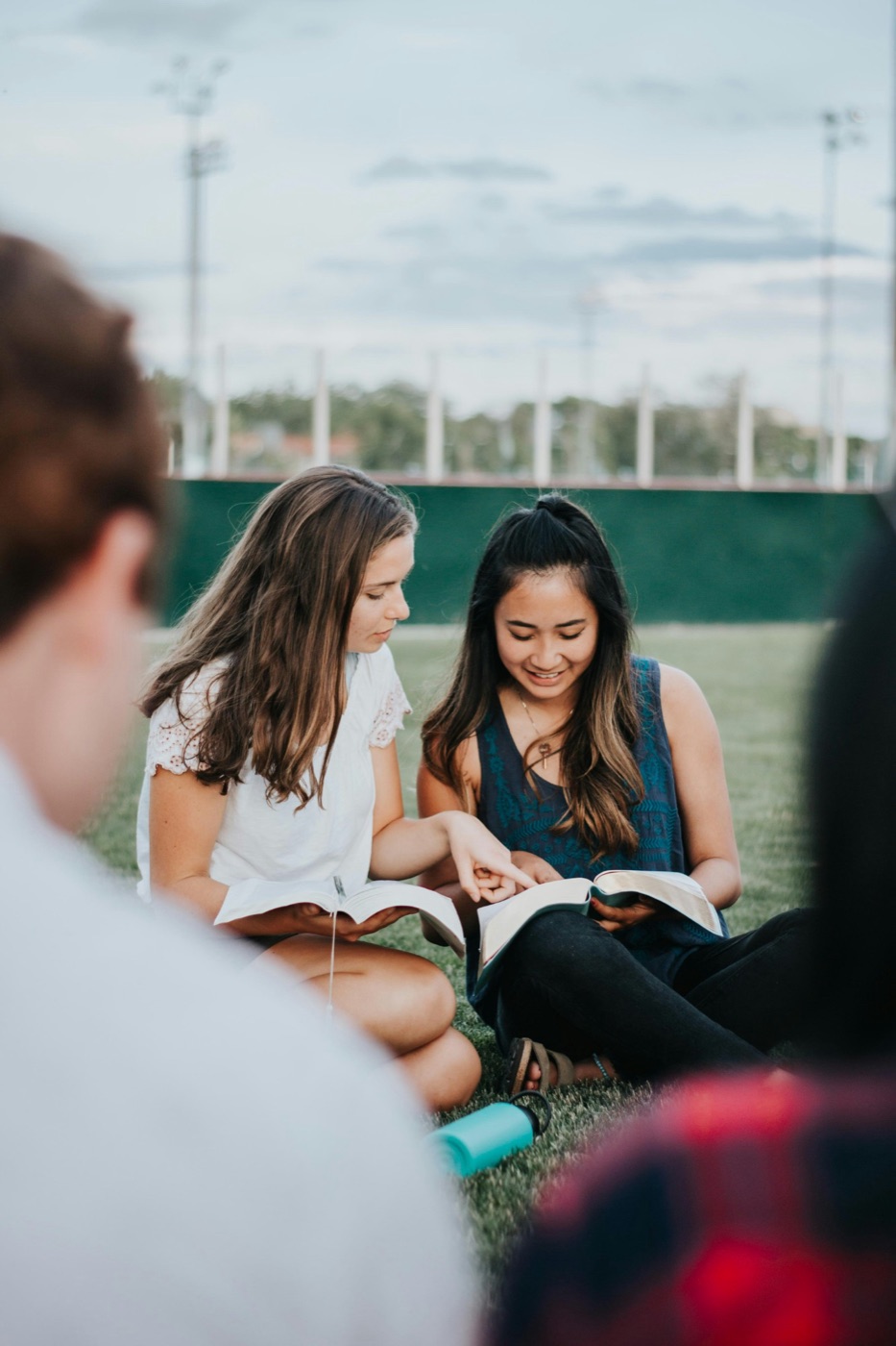 Two young women reading the Bible together on the grass